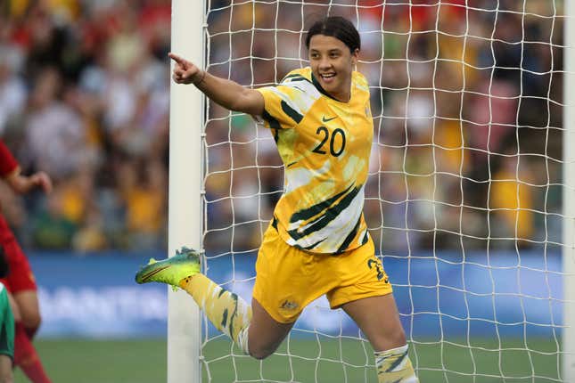 Sam Kerr of the Australian Matildas runs across the net and points her finger as she celebrates a goal, wearing a bright yellow jersey.