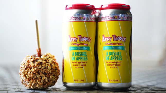 A caramel apple on a table beside two bright yellow cans of "A Bushel of Apples" beer