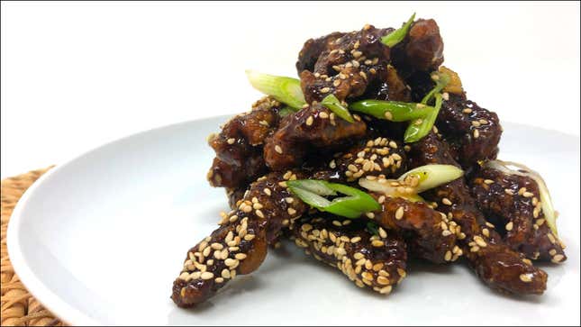 White plate with a pyramid stack of glazed beef tenderloin covered in scallions and sesame seeds