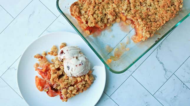 Peach crisp with oat topping and a scoop of ice cream next to dish full of peach crisp dessert.