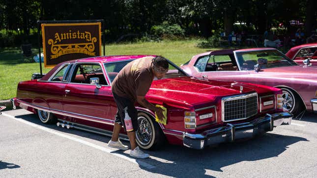 A car owner polishes their red car at a show. 