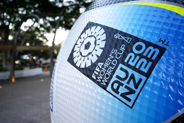 The side of a soccer ball that reads "FIFA Women's World Cup — AU-NX 2023" in various shades of blue is shown in an outdoors setting.