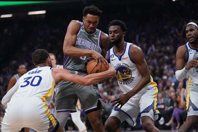 Apr 26, 2023; Sacramento, California, USA; Sacramento Kings guard Malik Monk (0) holds onto the ball next to Golden State Warriors guard Stephen Curry (30) and forward Andrew Wiggins (22) in the second quarter during game five of the 2023 NBA playoffs at the Golden 1 Center.