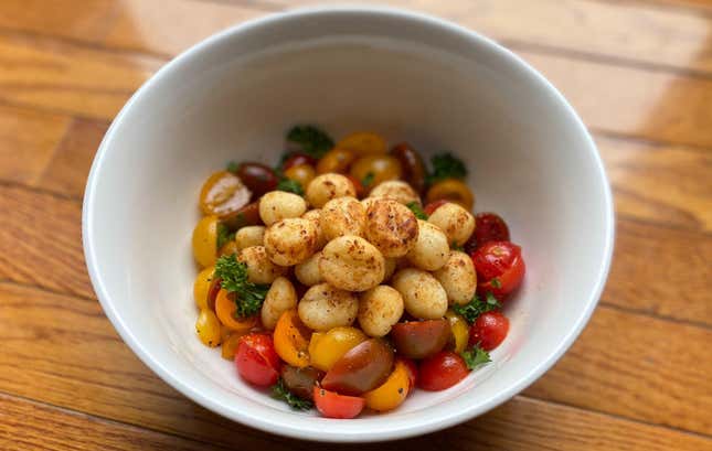 Bowl of air fried gnocchi with sliced cherry tomatoes and herbs