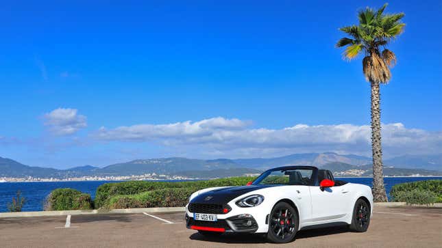 A photo of a white Abarth 124 Spyder next to a palm tree. 