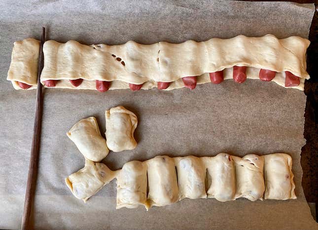 Mini hot dogs wrapped in dough and a chopstick pressing the dough between each dog.