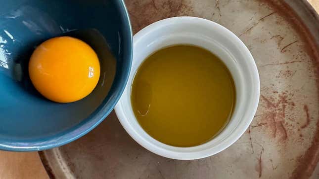 Egg yolk being lowered into ramekin of oil.