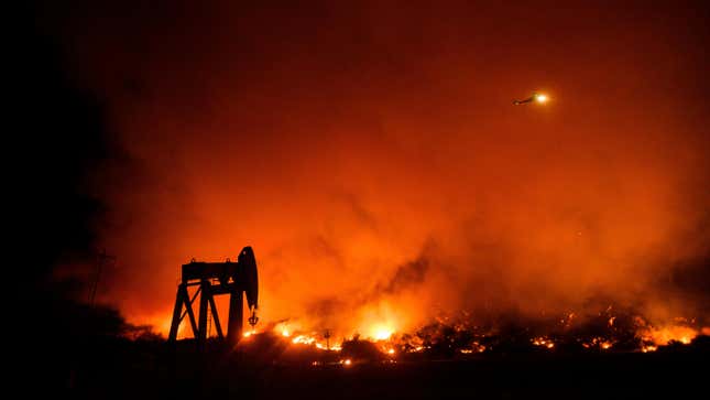 Smoke from the Maria Fire rises above an oil pumpjack as a helicopter passes overhead in the night. 