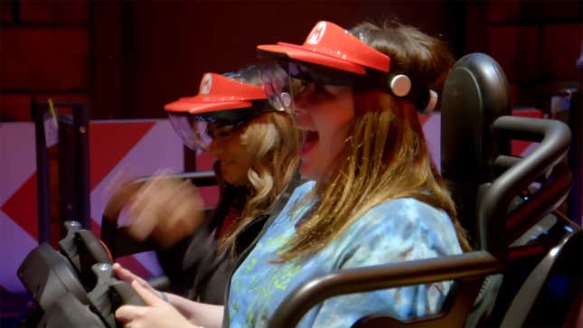 Two women wearing Mario-themed visors and goggles sit in a seat for the latest Mario Kart-themed ride at Universal Studios Hollywood theme park.