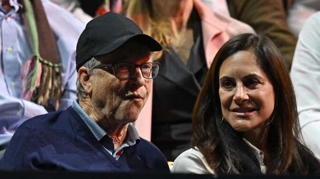 Bill Gates makes a face in a baseball cap while sitting in a crowd with his wife Melinda French Gates.