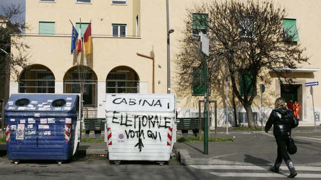 A woman walks past a trash bin defaced with graffiti (translation: “Electoral booth. Vote here”) in Rome.