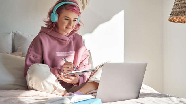 girl sitting on bed, studying with notes and laptop