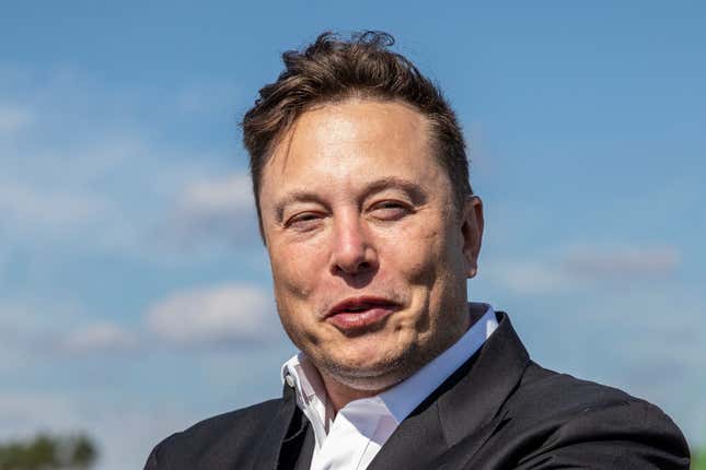 Elon Musk wearing a suit with no tie, squinting into the sun