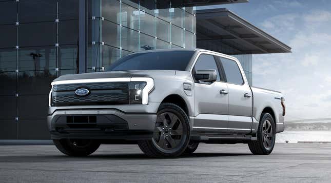 A silver 2023 Ford F-150 Lightning is parked in front of a glass building.