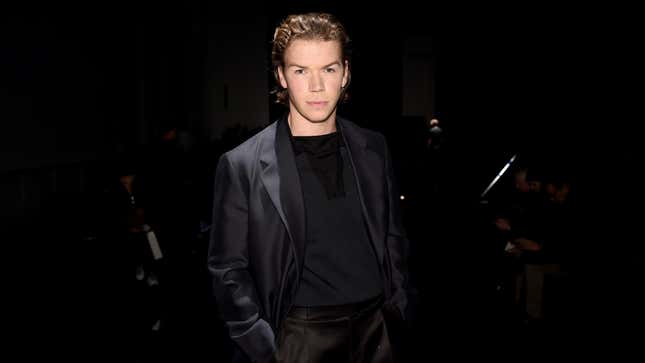 Will Poulter stands in a dark suit against a dark background at a red-carpet event.