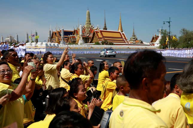 People wearing yellow, a color associated with both the current monarch and his father, cheer as the motorcade carrying king Maha Vajiralongkorn and queen Suthida drives past the Grand Palace in Bangkok.