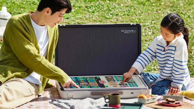 Two people in a park having a picnic using the LG StanbyME with its screen laid flat to play a digital board game.