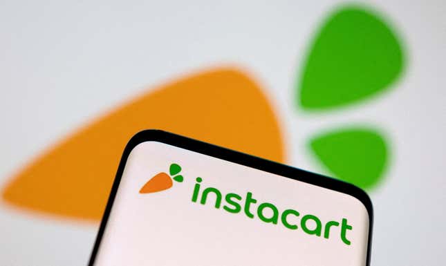 An image of a phone with the carrot-like Instacart logo, held in front of a background showing a blurry Instacart logo.