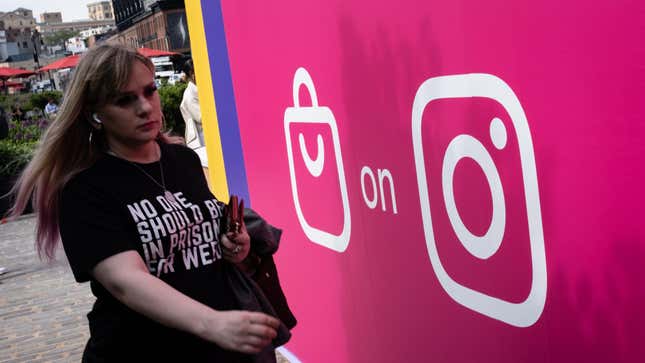 A woman wearing a black t shirt walks by a wall sporting a shopping bag symbol and the Instagram logo.