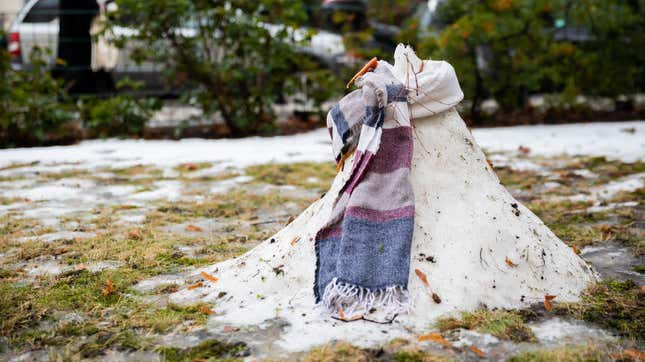 A melting snowman wearing a scarf surrounded by dirt