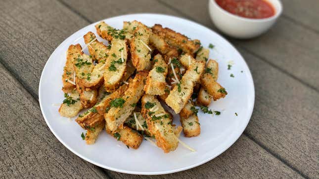 Plate of garlic bread fries topped with parsley, beside a bowl of marinara dipping sauce
