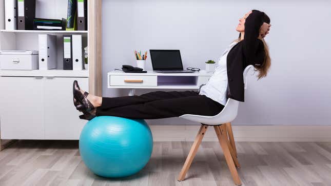 Woman at her desk with a chair and a yoga ball (her feet are propped up on the yoga ball)