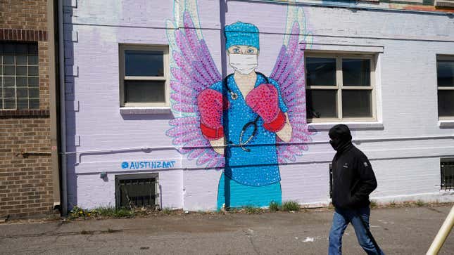 A man in a mask walks by a mural depicting a medical worker with a mask covering her mouth and nose, wearing boxing gloves and angel-like wings on her back on April 14, 2020, in downtown Denver.