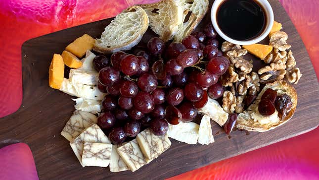 Overhead view of a cheese board with pickled red grapes, cheese, bread, and walnuts