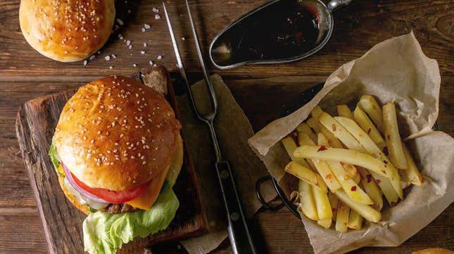 Flatlay shot of burger with sesame bun and fries on wooden background