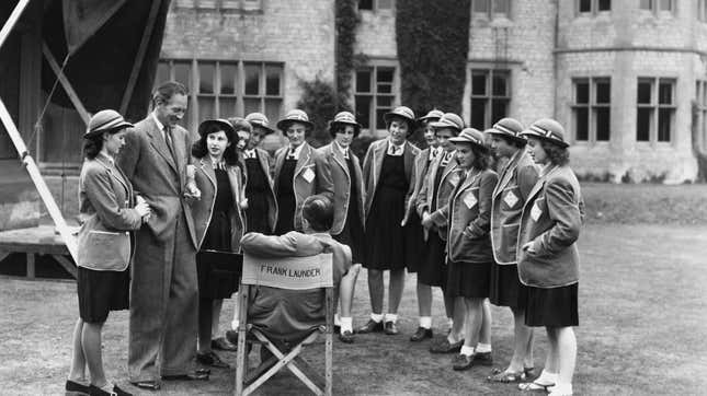 British filmmaker Frank Launder (1906- 1997, seated, centre) with actor Guy Middleton and a group of schoolgirl extras at Langley Court, Liss, Hampshire during filming of the comedy ‘The Happiest Days of Your Life’, 19th September 1949. 