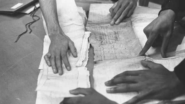 circa 1960: At the Schomburg Center for Research in Black Culture, in New York’s public library, the hands of a group of scholars piece together a ship’s document about a cargo of slaves brought to the United States.