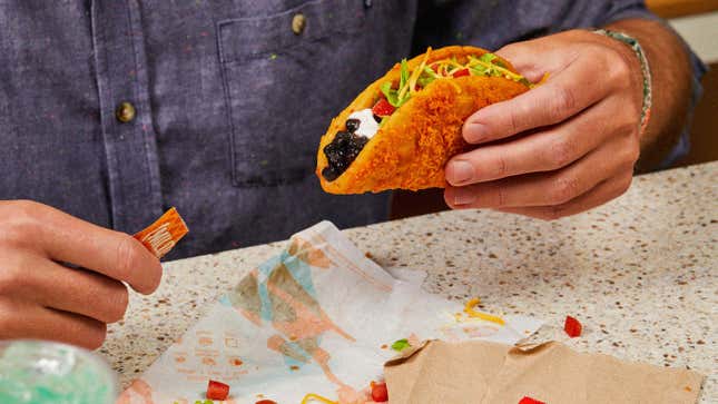 Hand holding the Toasted Cheddar Chalupa with black beans, adding mild hot sauce