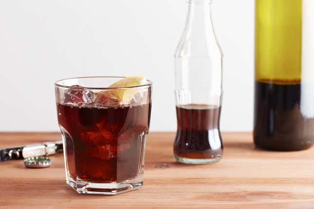 Kalimotxo in glass beside soda bottle and red wine bottle on countertop
