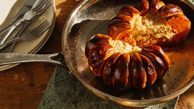 Roasted stuffed pumpkin sliced down the middle sitting in a skillet on top of a wooden table