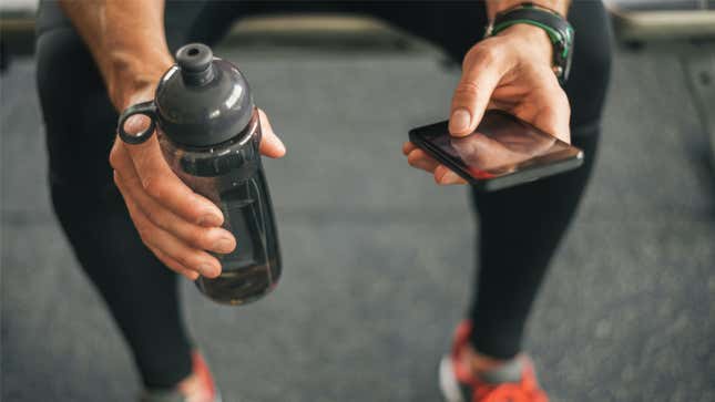 person holding a water bottle and phone at the gym