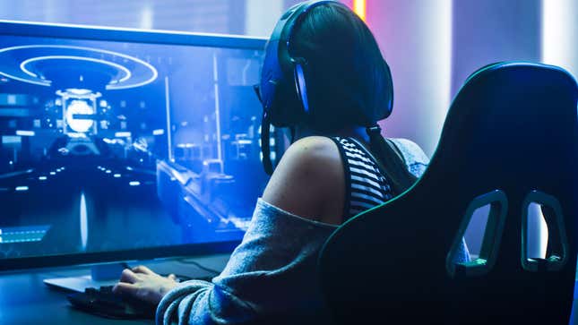 A woman sits at a computer playing a game while wearing a headset