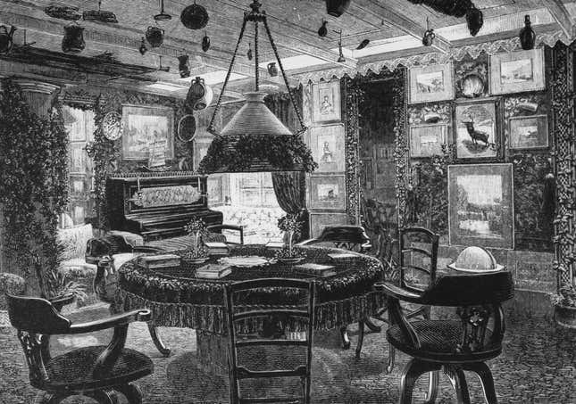 A Victorian parlor, furnished with a round table, swivel chairs, a selection of paintings and a piano, circa 1890.
