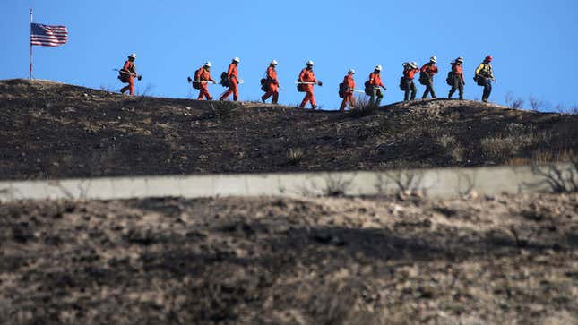 Inmate firefighters march past an American flag, while led by a fire captain, as they work to put out hot spots from the Tick Fire on October 25, 2019 in Canyon Country, California.
