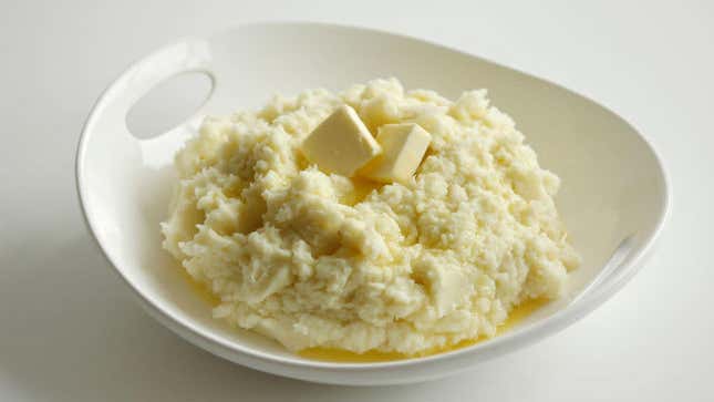 Mashed potatoes topped with butter in a white dish on a white background