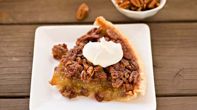 Slice of pecan pie with whipped cream on a white plate