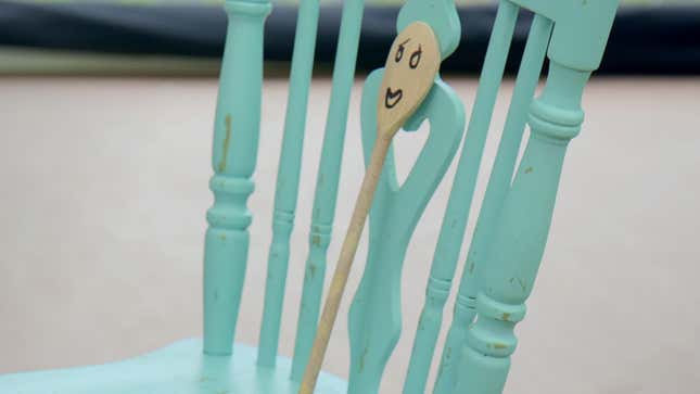 a wooden spoon with a face drawn on it, sitting on a wooden chair