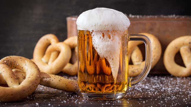 Foamy pint glass of beer surrounded by pretzels