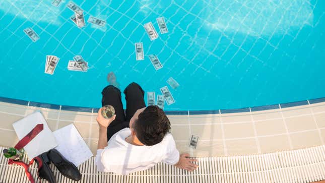 A man sits on the edge of a pool with his feet in the water and a glass in his left hand. There are dollar bills floating in the water.