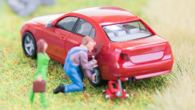 A toy man changes a tire on a model car
