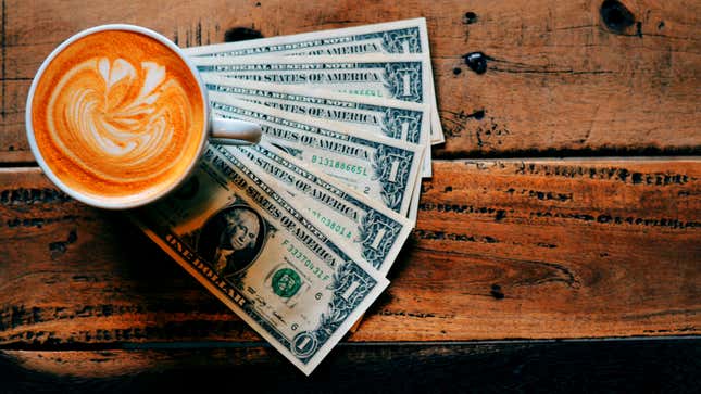 A latte in a mug sitting next to a stack of dollar bills