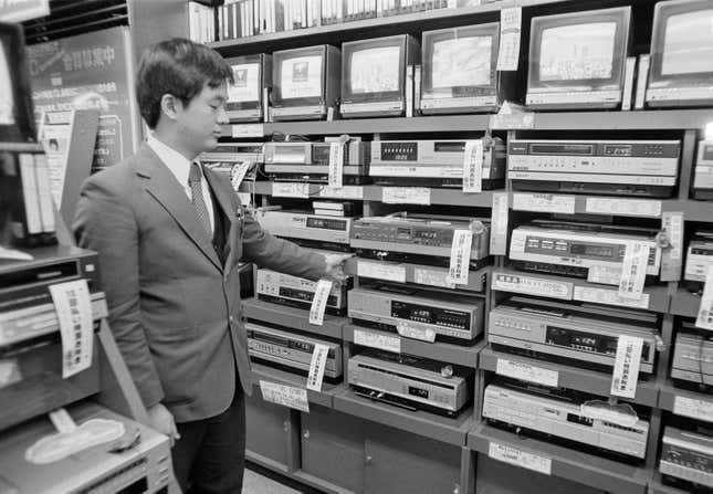 A sales clerk at an electronics store in the Akihabara district of Tokyo, Japan, displays a stack of video cassette recorders (VCR), which are on sale for 20 to 30 percent off, Dec. 15, 1981.