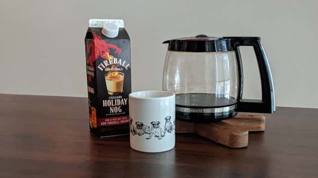 Carton of Fireball holiday nog, a coffee mug, and a pot of coffee on a wooden table
