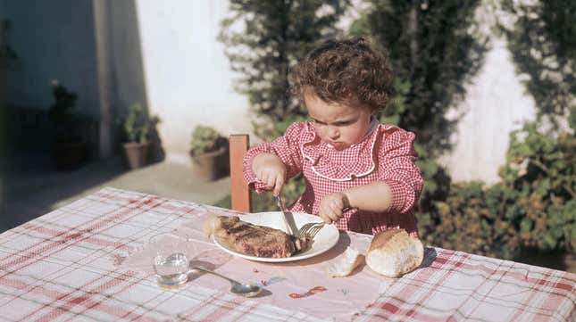 Little girl cutting into large steak with fork and knife