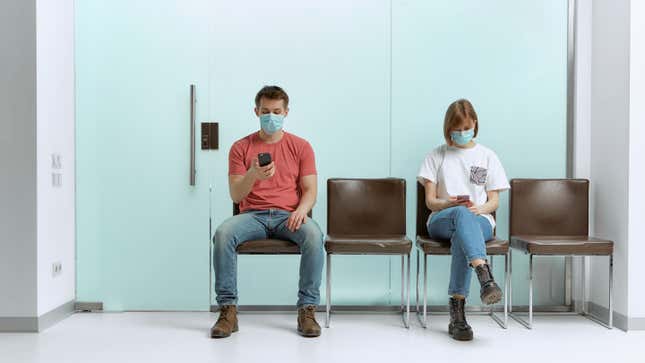 two people in masks sitting in a waiting room