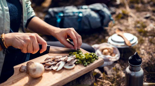 hands chopping mushrooms outdoors on a plank